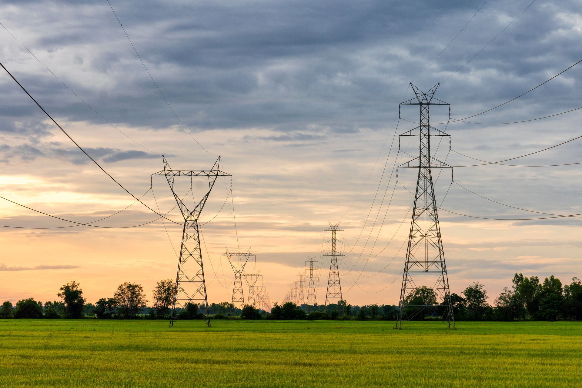 Power lines and towers against a cloudy sunset over a green field.