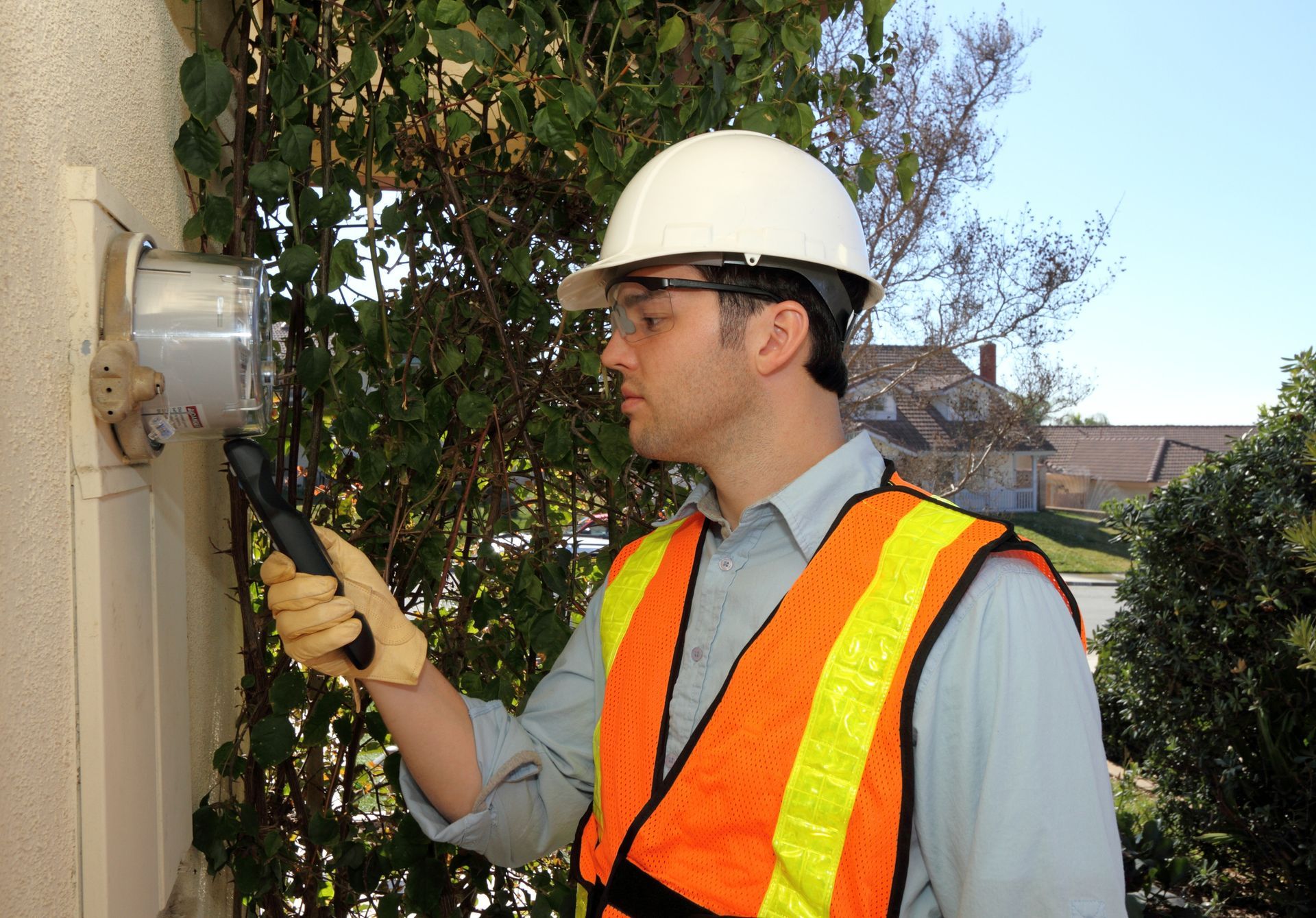 An emergency electrician in a safety vest & glasses works on fixing an electrical meter for safety. An emergency electrician in a safety vest & glasses works on fixing an electrical meter for safety.