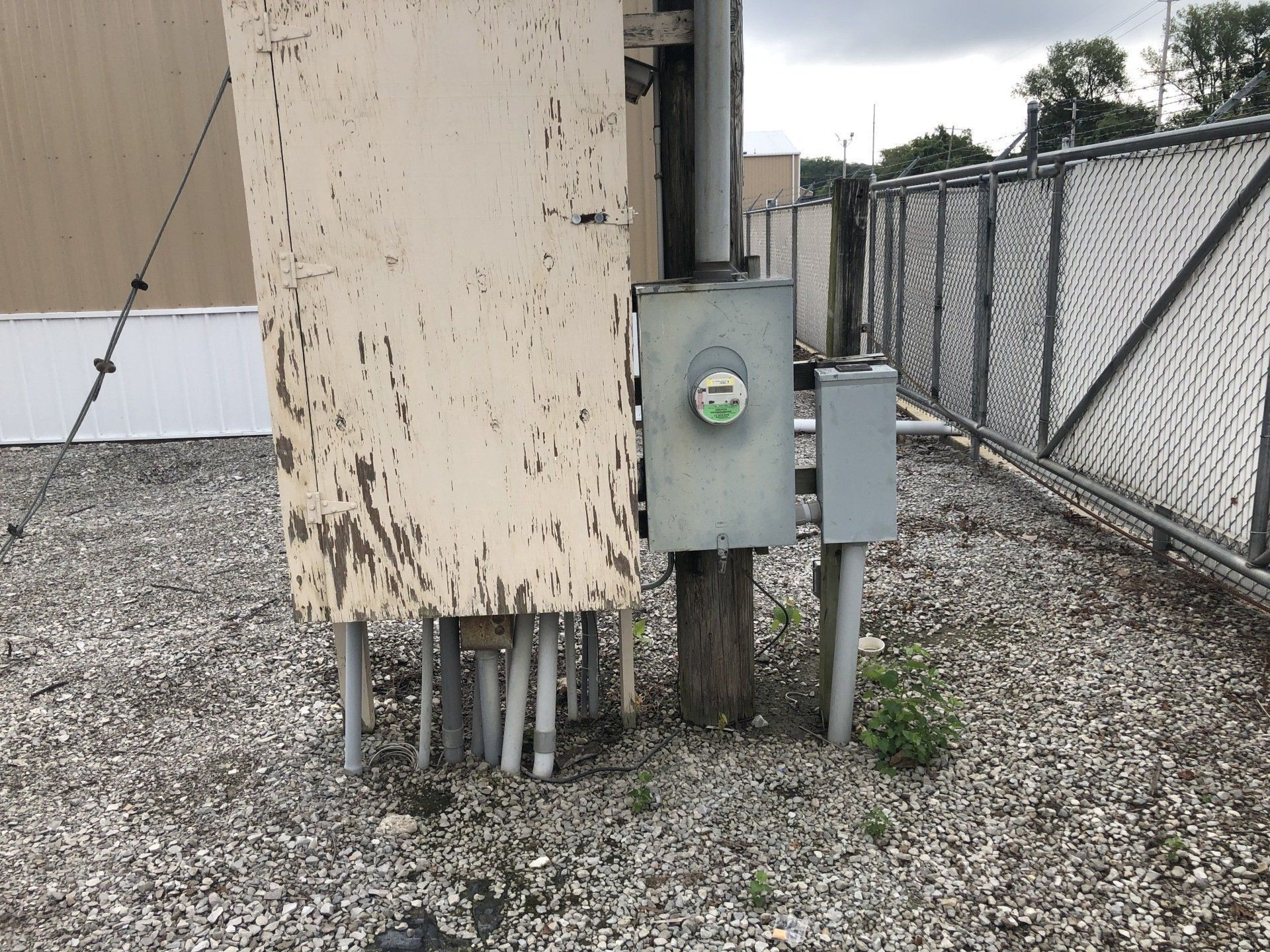 A dirty electrical box is sitting on the ground next to a chain link fence.