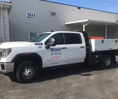 White work truck with a flatbed parked in front of a building with the number 2511.
