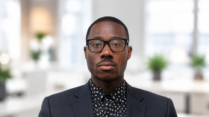 Portrait of a man in glasses and a dark blazer against a bright office background