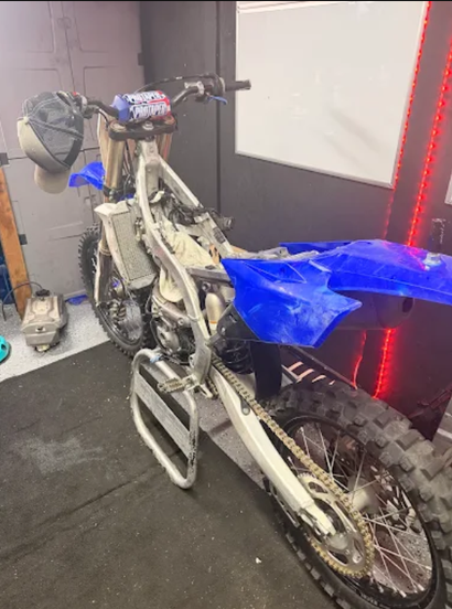 Dirt bike with blue seat cover parked indoors on a dark floor near a wall with red LED lights