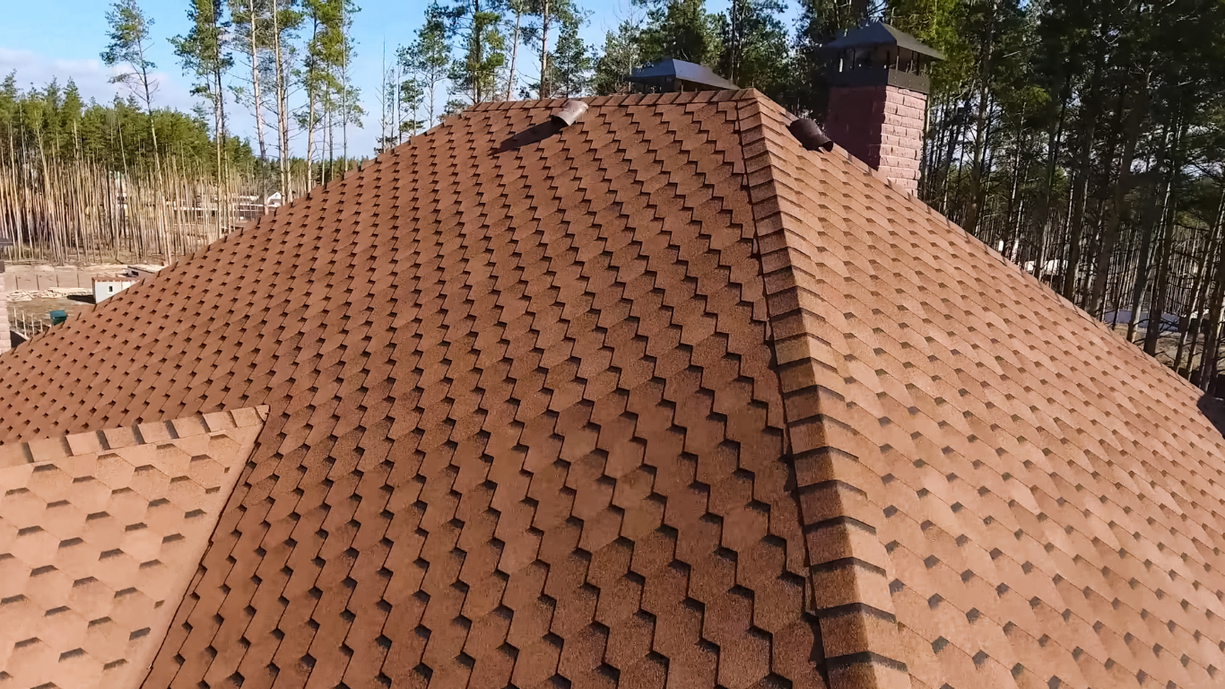 Brown shingle roof on a house, viewed from above with trees in the background