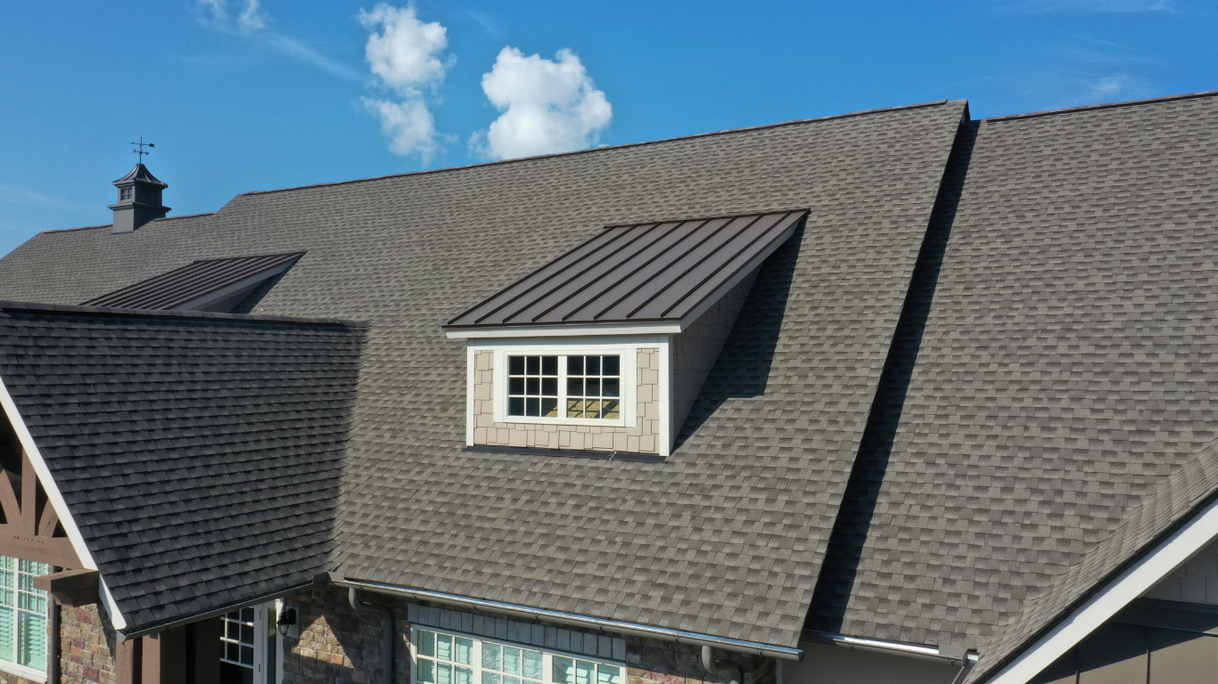 Dark gray shingled house roof with dormer windows under a blue sky with clouds