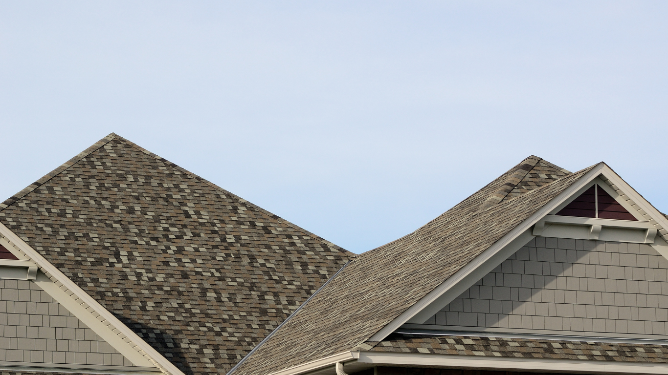 Two adjacent house rooftops with gray shingles against a pale sky