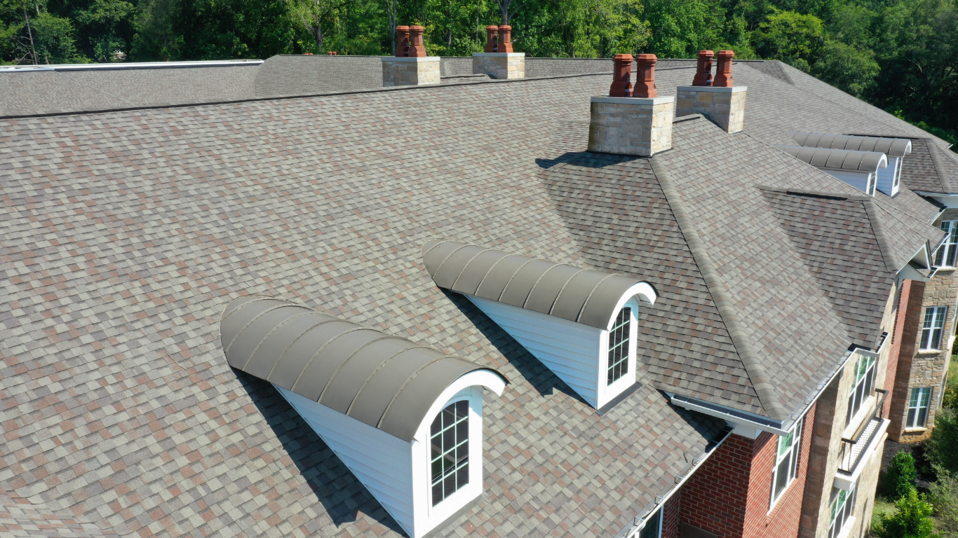Aerial view of a house roof with two small dormer windows and several chimneys.