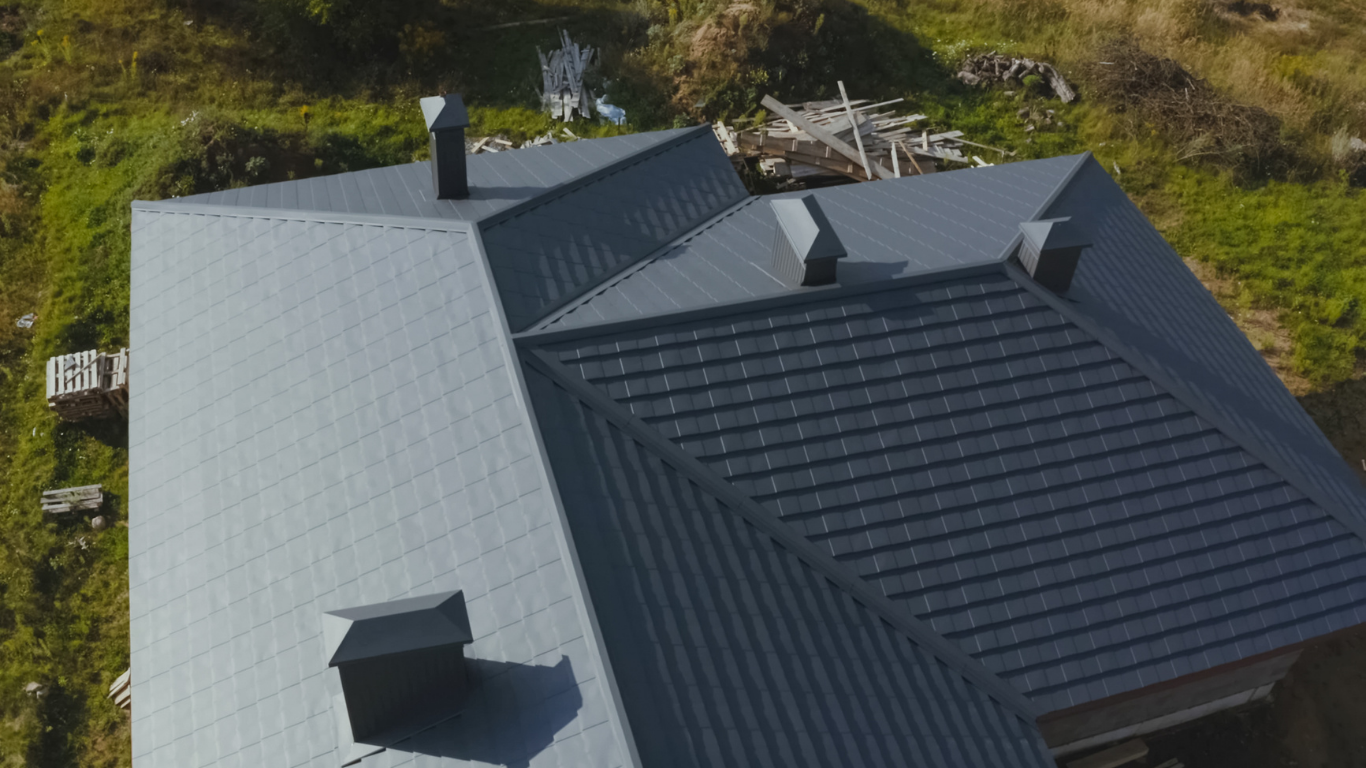 Aerial view of a house roof with gray shingles and skylights, surrounded by trees.