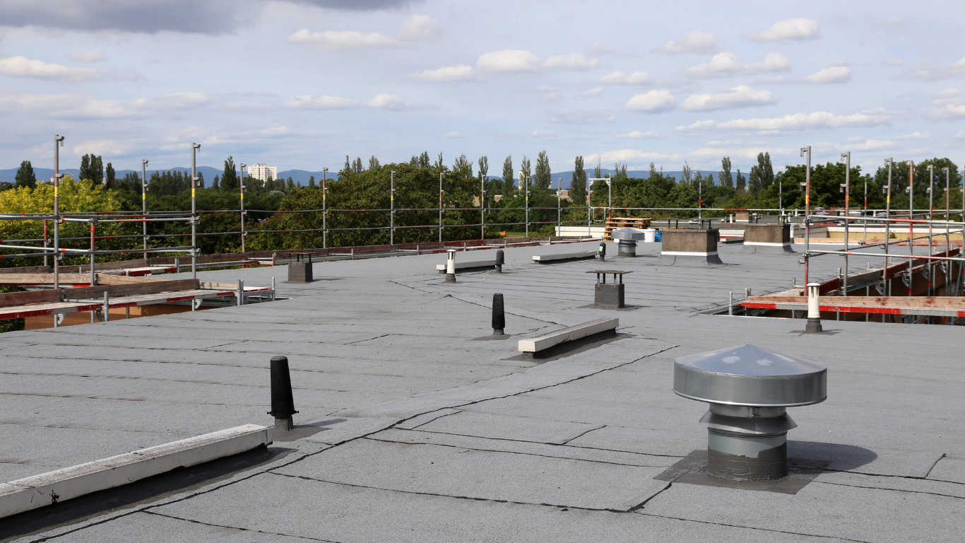 Flat rooftop with vents and railing under a cloudy sky.