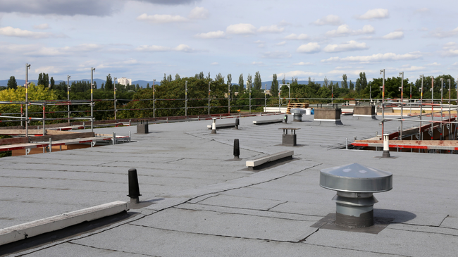 Flat rooftop with vents and low parapet walls under a cloudy sky, with trees in the distance