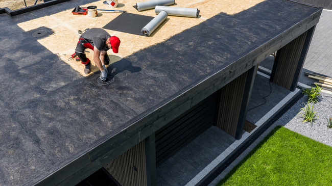 Worker installing roofing on a flat roof beside HVAC units