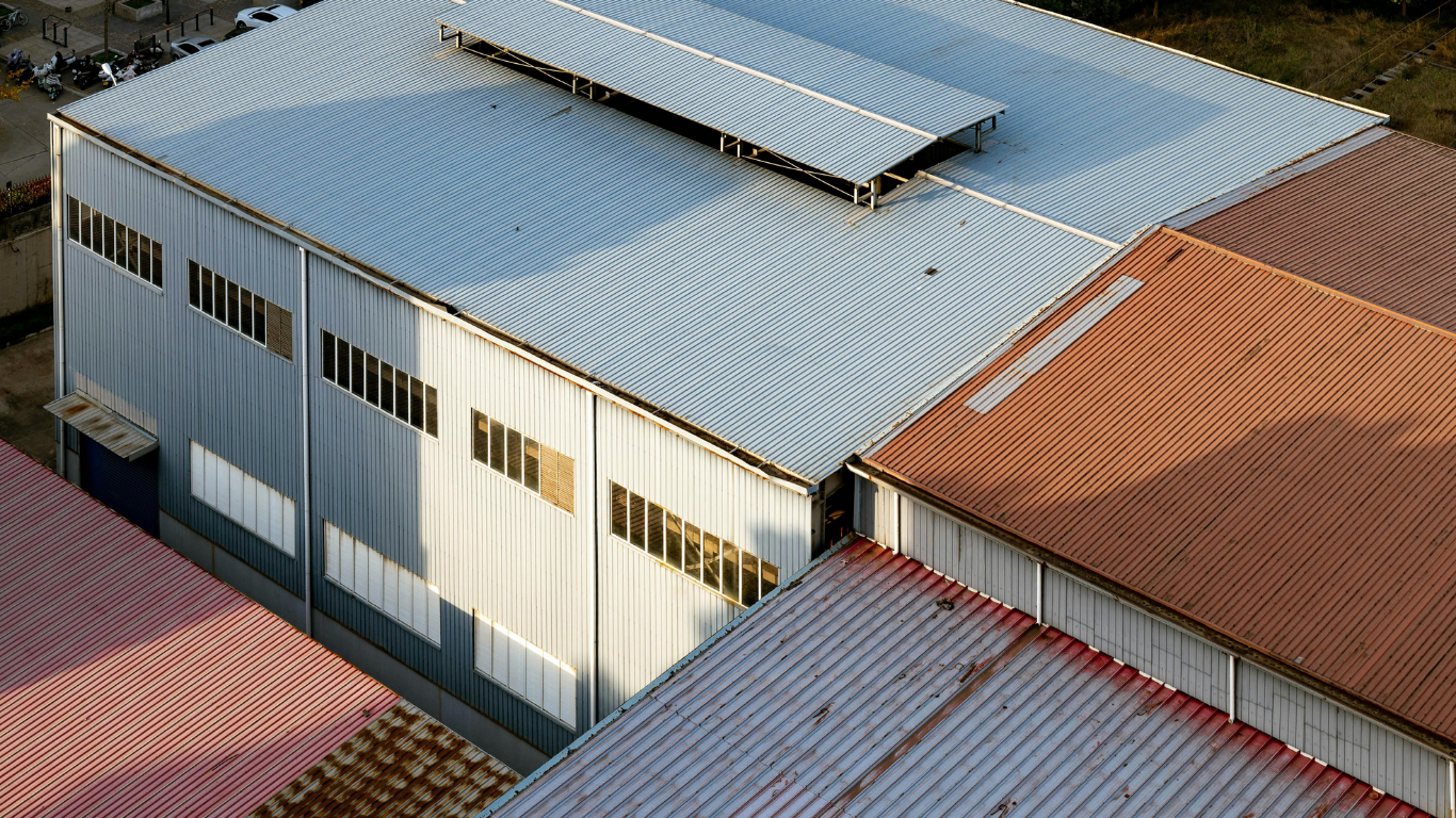 Aerial view of metal-roofed industrial buildings with skylights and rust-colored sections.