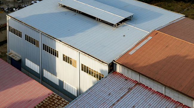 Aerial view of industrial warehouse roofs with white and rust-colored metal panels.