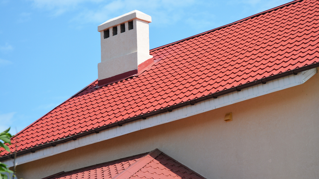 Red-tiled roof with a white chimney against a clear blue sky