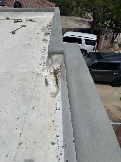 Rooftop with cracked white surface and damaged parapet wall overlooking parked vehicles below