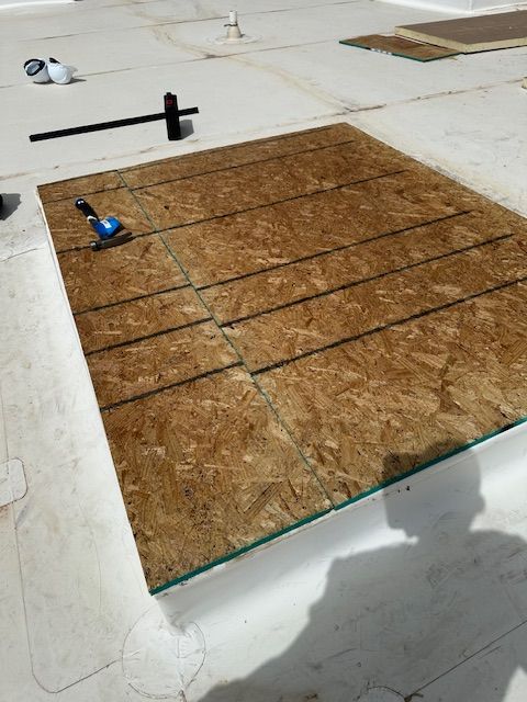 Roofing work area with brown plywood sheathing, tools, and a hammer on a flat roof.
