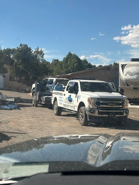 White utility trucks parked on a gravel lot beside a building under a blue sky