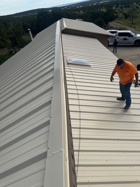 Worker inspecting a metal roof on a sloped rooftop with a skylight in daylight