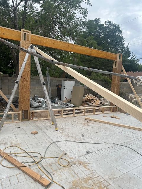 Construction site with wooden framing, angled braces, and tools on a concrete floor under cloudy trees