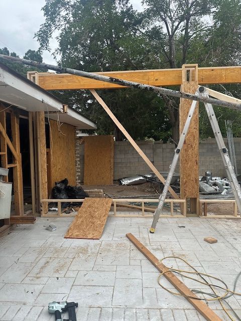 Partially built house with roof framing, lumber supports, and construction tools in a paved courtyard