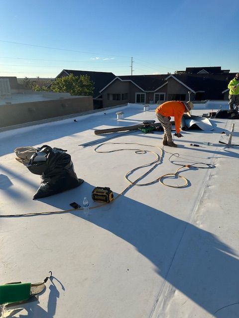 Workers installing equipment on a flat rooftop, with tools, cables, and bright sunlight.
