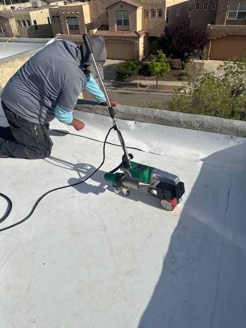 Worker cleaning a white rooftop with a green pressure washer near suburban houses