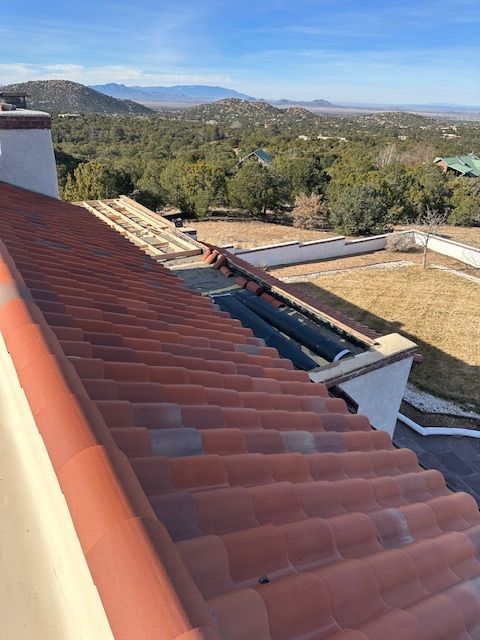 Red tile roof with damaged section overlooking a wooded hillside and distant mountains
