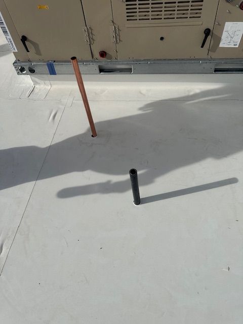 Snow-covered rooftop with a building wall and two upright pipes casting long shadows.