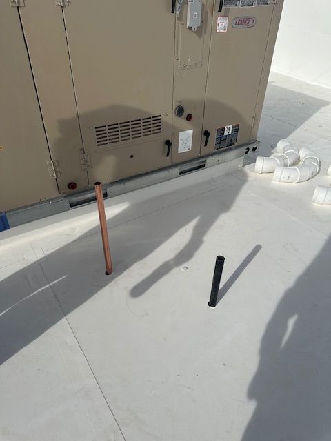 Roof HVAC unit with two metal rods standing on a white rooftop, casting shadows.
