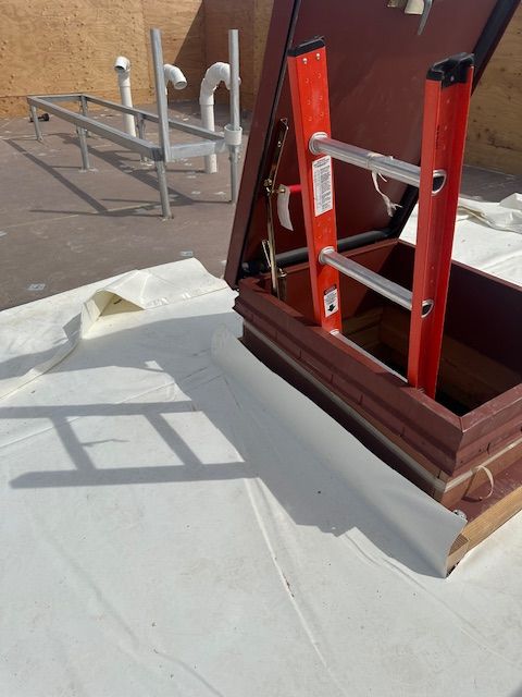 Red ladder and rooftop equipment beside a white tarp-covered surface casting a ladder-shaped shadow.