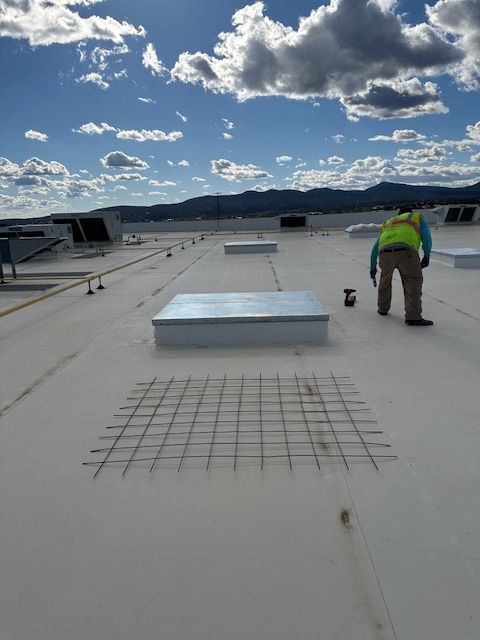 Worker inspecting a flat rooftop with vents under a cloudy sky and mountains in the distance