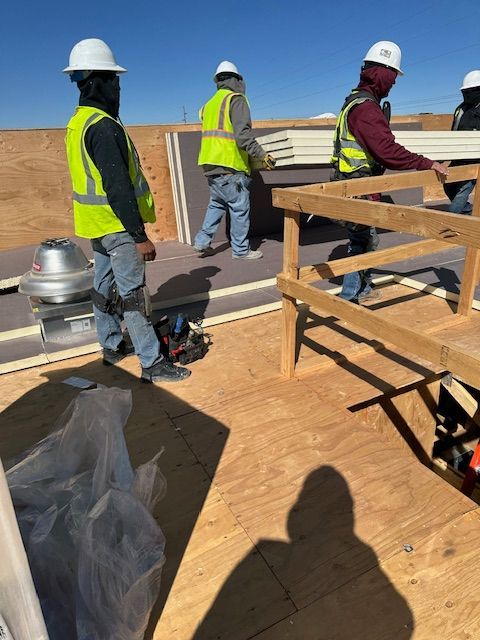 Construction workers in hard hats and safety vests on a rooftop, working beside a wooden frame.