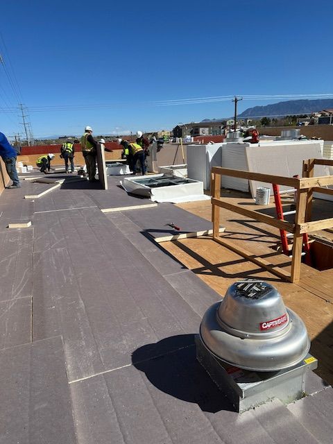 Workers on a rooftop with construction materials and a silver vent under a clear blue sky