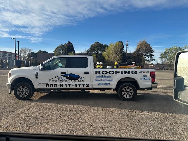 White roofing company pickup truck with logo and phone number parked on a sunny street.