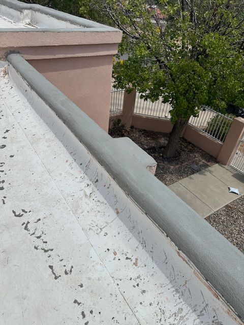 Rooftop with white parapet wall, beige building edge, and trees in a courtyard below.