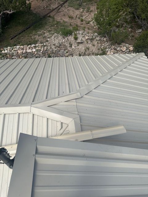 White metal roof with a bent panel and surrounding gravel yard.