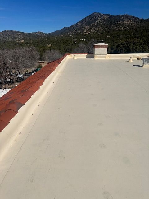 Rooftop with white coating and red edge, overlooking mountains under a clear blue sky.