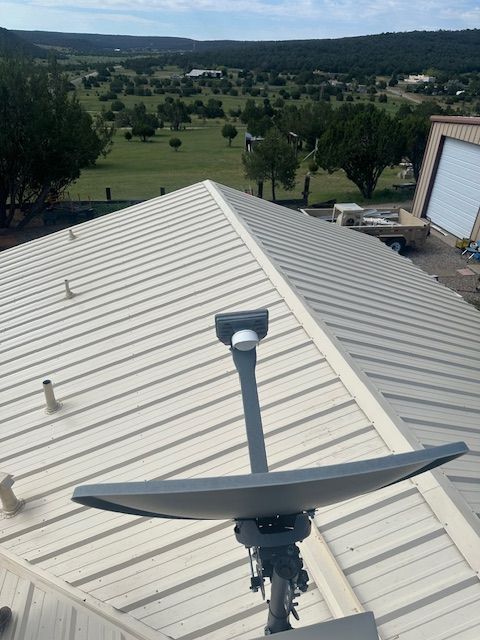 Satellite dish on a metal roof overlooking a green valley and distant hills.