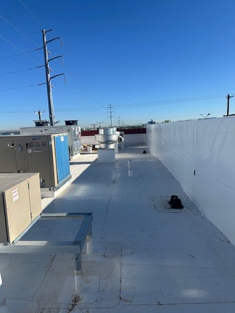Rooftop with white coating, HVAC units, utility poles, and a clear blue sky.