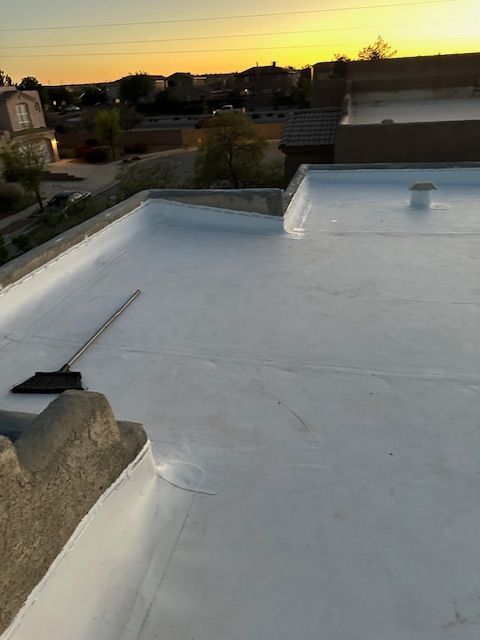 White flat rooftop at sunset with a broom and distant houses under a glowing sky