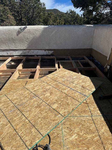 Roof under construction with plywood decking and concrete parapet walls under a clear sky