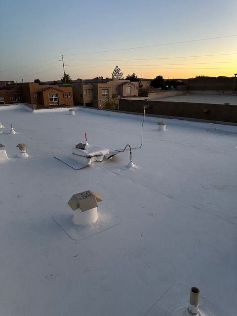 Flat white rooftop at sunset with vents and antennas, city buildings silhouetted in the background.