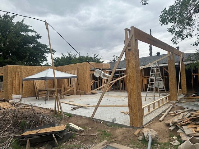 Construction site with wooden framing, ladders, and a white canopy under cloudy skies