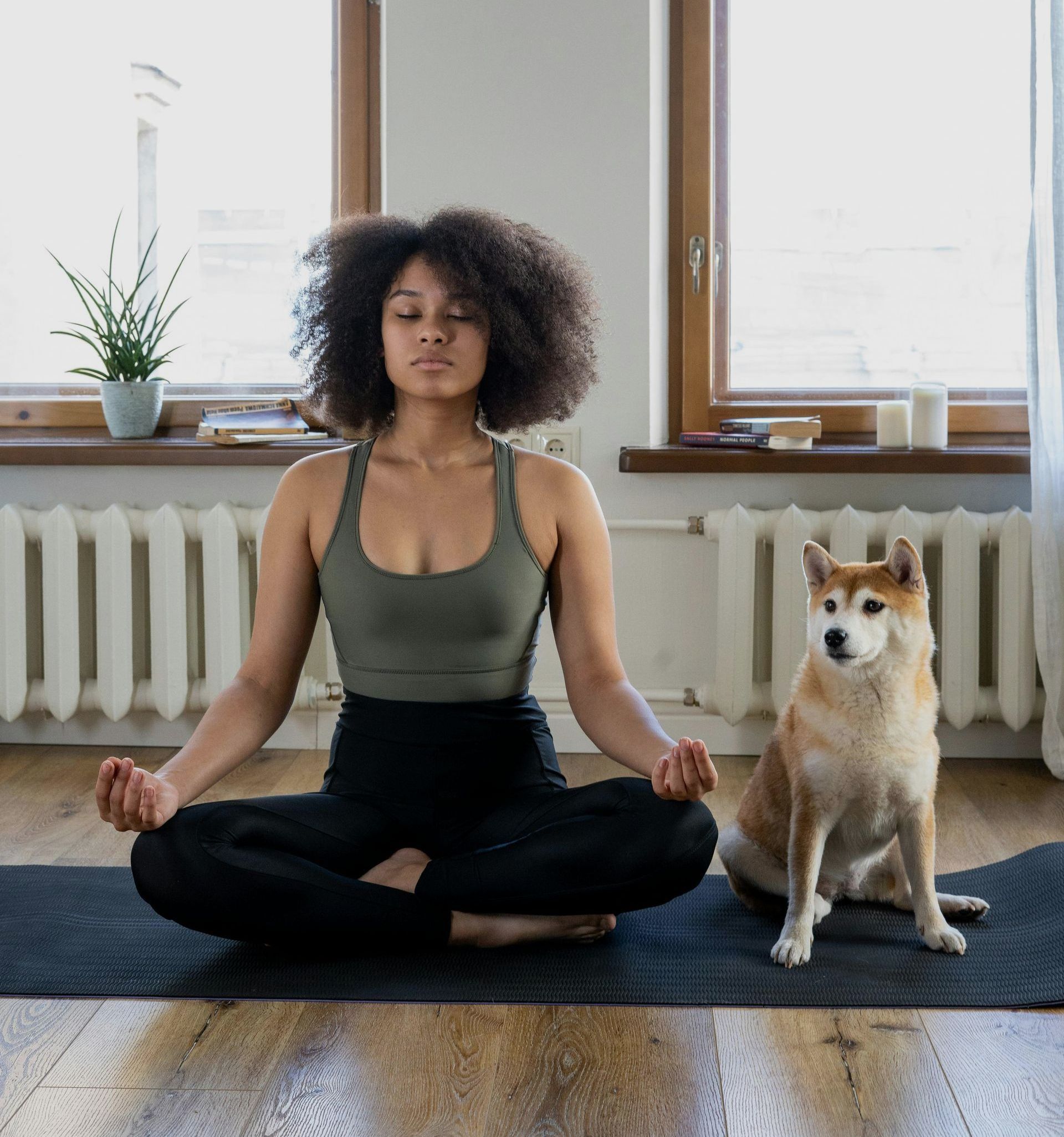 A woman is sitting on a yoga mat next to a dog.