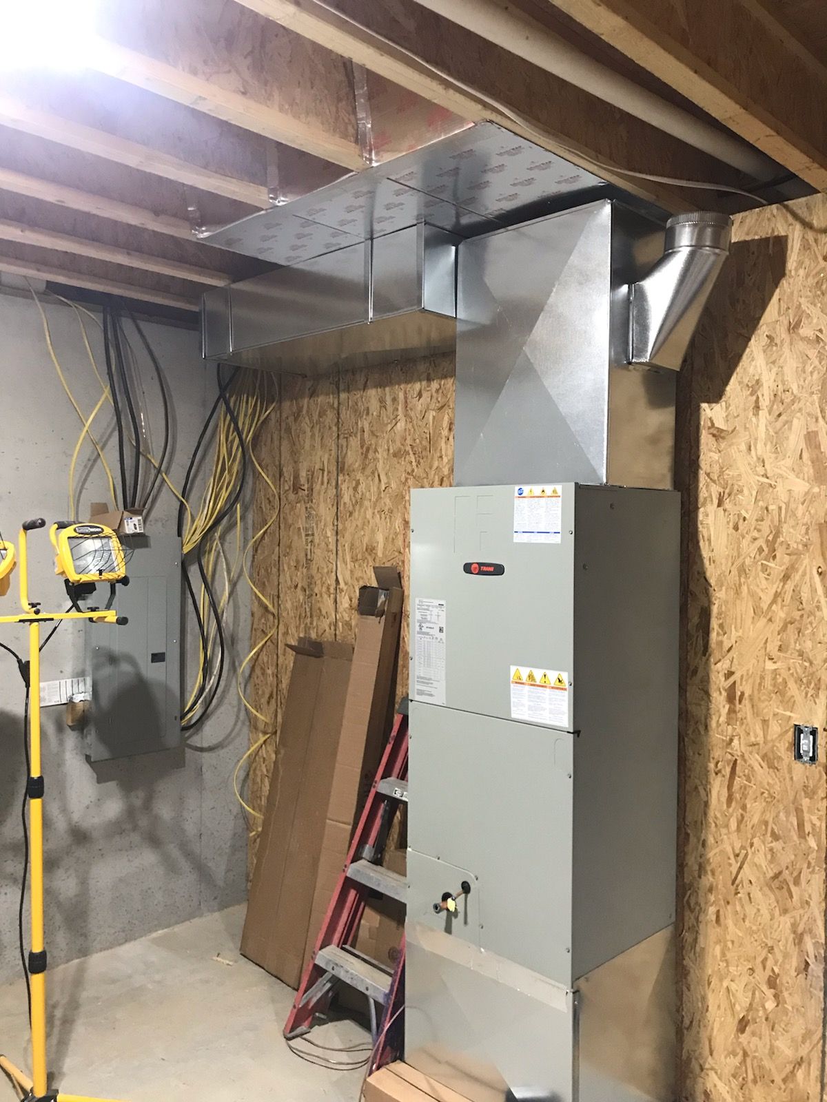 HVAC unit and ductwork in unfinished basement, near electrical panel. Wooden paneling on wall.