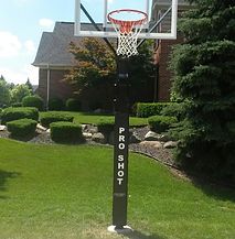 A basketball hoop is sitting in the grass in front of a house.