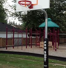A basketball hoop in a park with a playground in the background.
