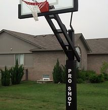 A basketball hoop is sitting in the grass in front of a house.