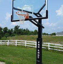 A basketball hoop is sitting in the middle of a grassy field next to a fence.