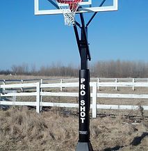 A basketball hoop is sitting in the middle of a field next to a white fence.