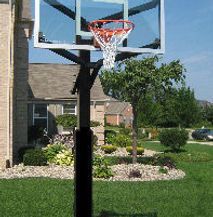 A basketball hoop is sitting in the grass in front of a house.
